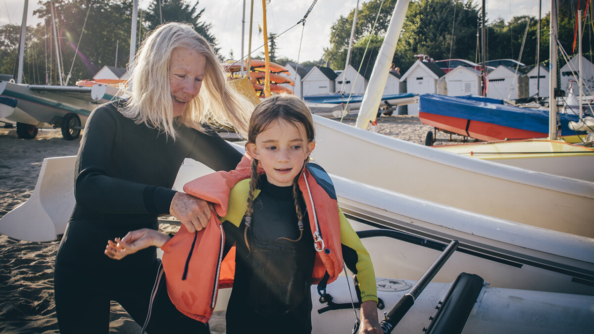 Little girl receiving a helping hand from her grandmother to get her lifejacket on.