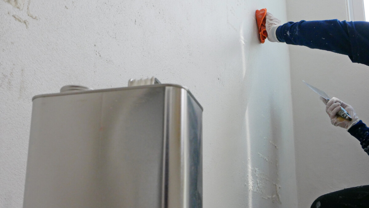 A hand of a painter holding on a piece of cloth, soaked with thinner, removing sticky rough glue and tape remain on the old concrete wall, as a preparation before starting the paint the house