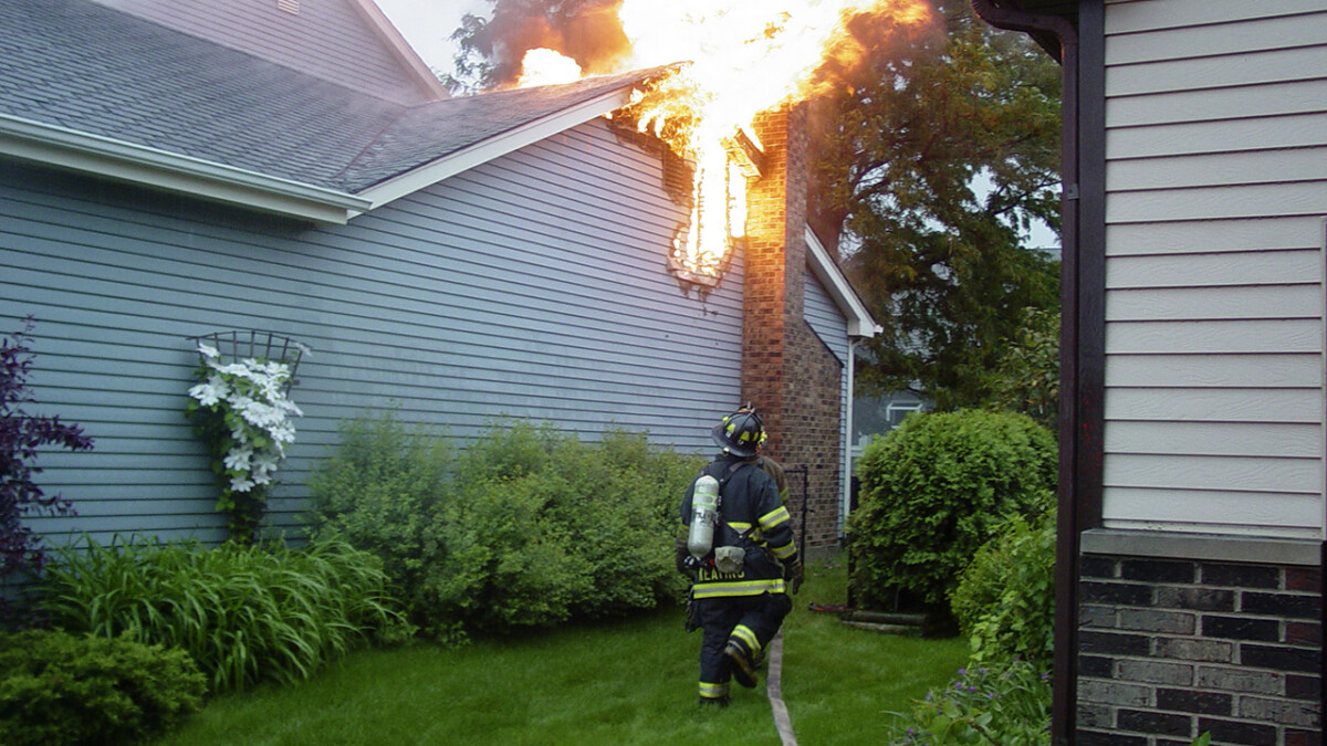 The roof of a house is burning, while a firefighter rushes with his hose to put out the blaze.