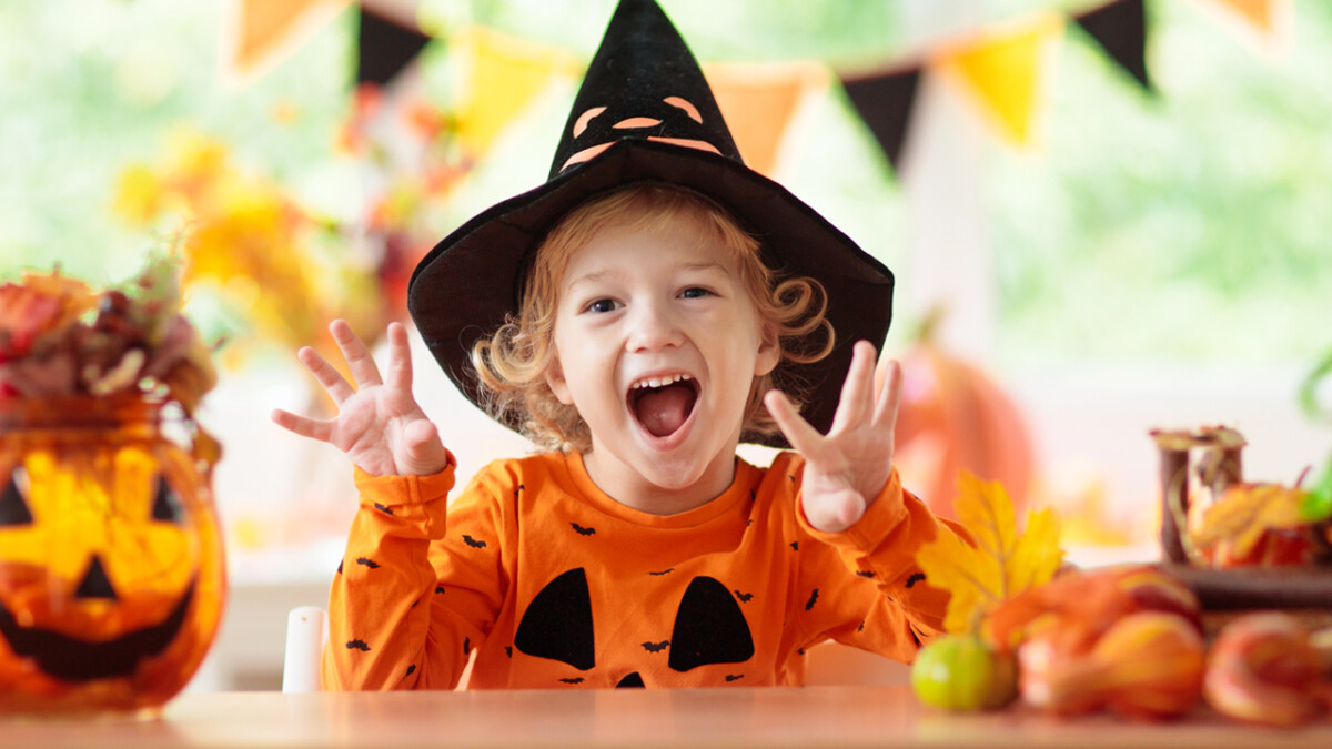 Child in Halloween costume. Kids trick or treat. Little boy with pumpkin lantern. Baby in witch hat. Autumn season holiday decoration. Home festive interior with fall leaves and squash.